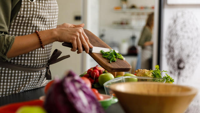 Woman putting a spring onion she chopped in a glass baking tray 